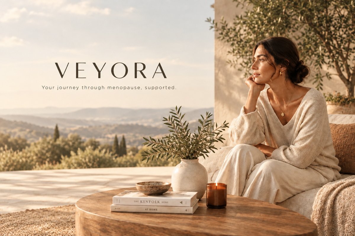 VEYORA – Your journey through menopause, supported. A woman in a cream knit lounge set relaxing on a sunny terrace overlooking the countryside.